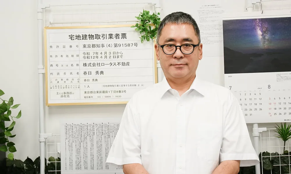 宅地建物取引業者票の前に立つ、代表 春日の写真